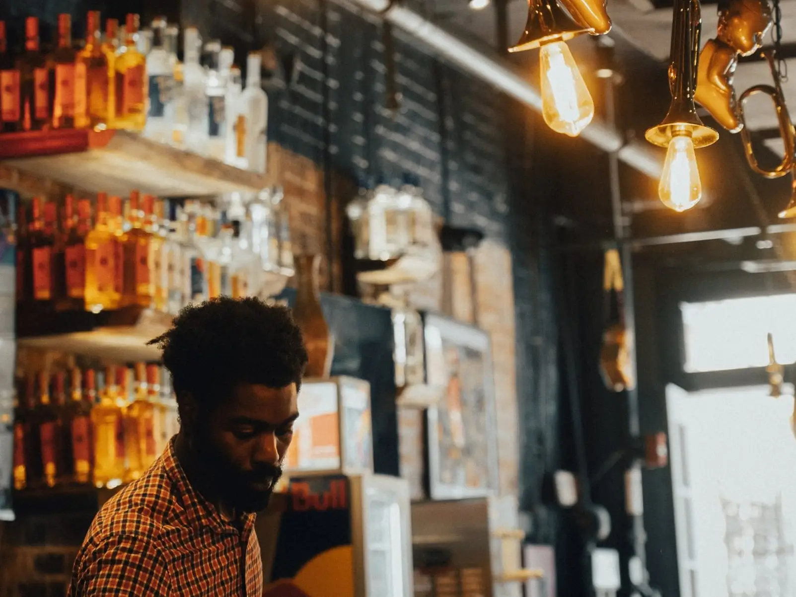 A bartender at work under hanging brass trumpets and Edison bulbs