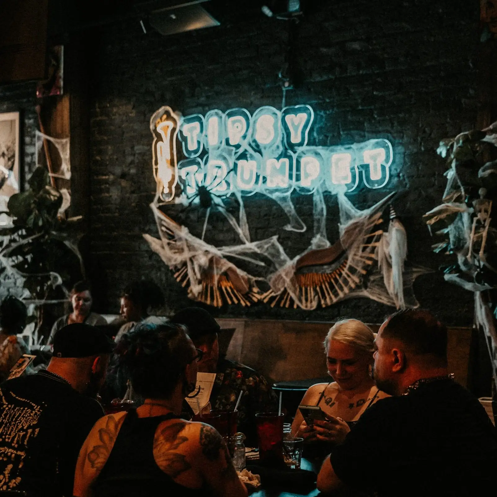 A full room of guests at tables under the Tipsy Trumpet neon sign
