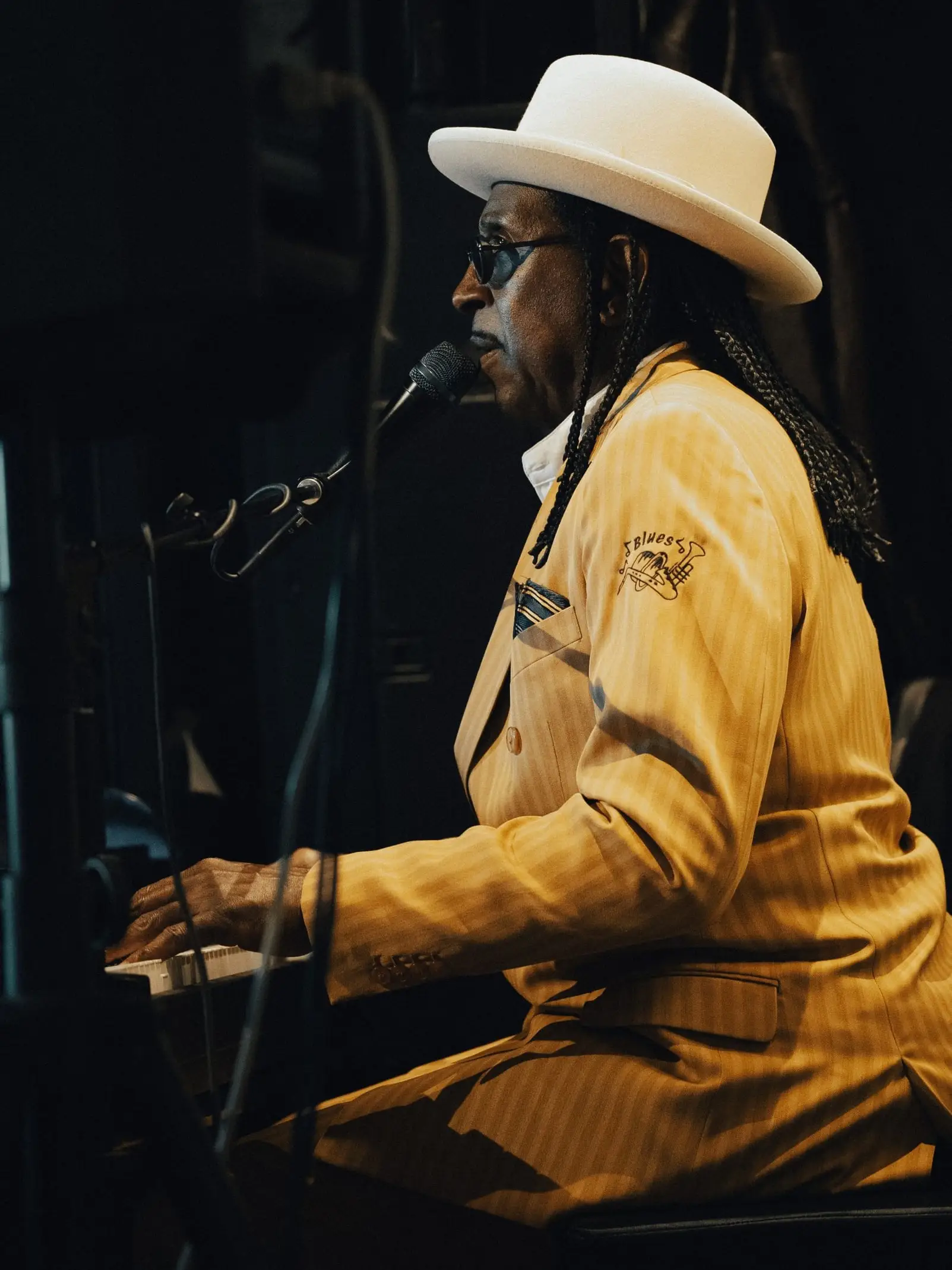 A pianist in a yellow suit and white hat sings at the keys