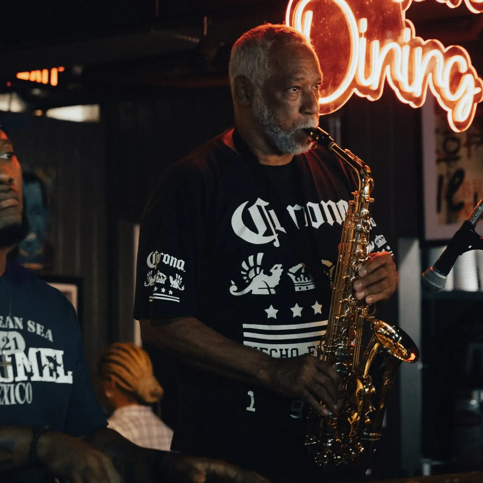 A saxophonist plays under a red “Courtyard Dining” neon sign