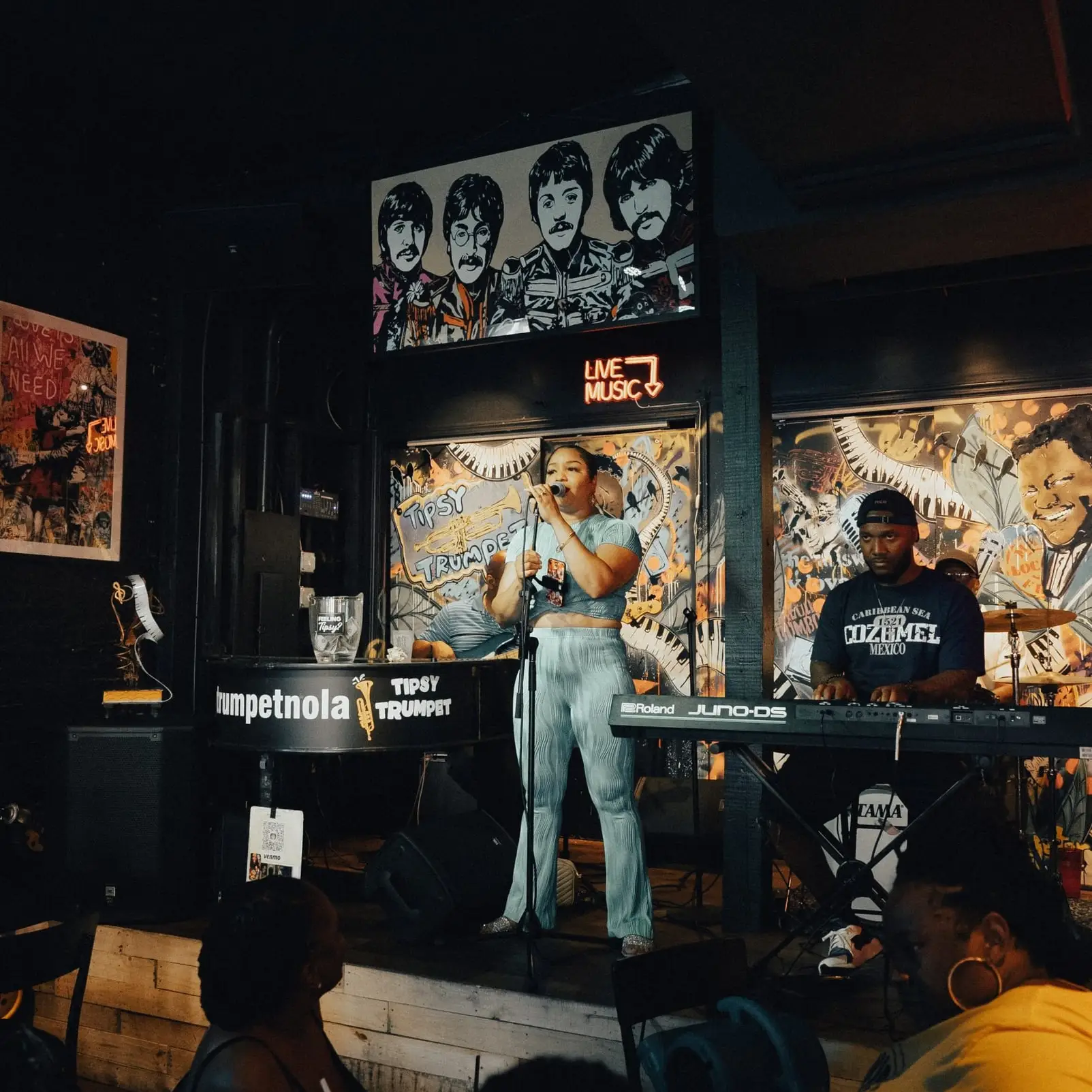 A singer and a keyboardist perform on the stage, with guests watching from their tables